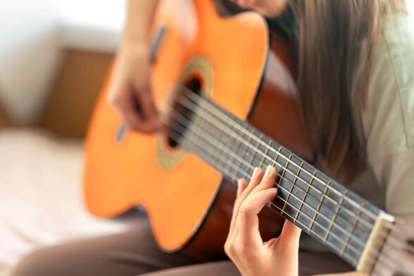 Gros plan sur les mains d'un musicien jouant de la guitare classique, doigts positionnés sur le manche
